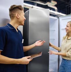Engaging Customer Service: Young Salesperson Assisting Shopper in Appliance Store In a modern appliance store, an enthusiastic young salesperson helps a curious customer explore various refrigerators, highlighting their unique features during the shopping experience
