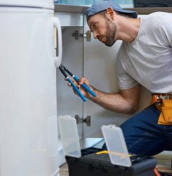 Professional repairman looking focused, using pipe wrench while examining and fixing sink pipe in the kitchen Professional repairman looking focused, using pipe wrench while examining and fixing sink pipe in the kitchen. Repair service and plumbing concept. Side view. Vertical shot